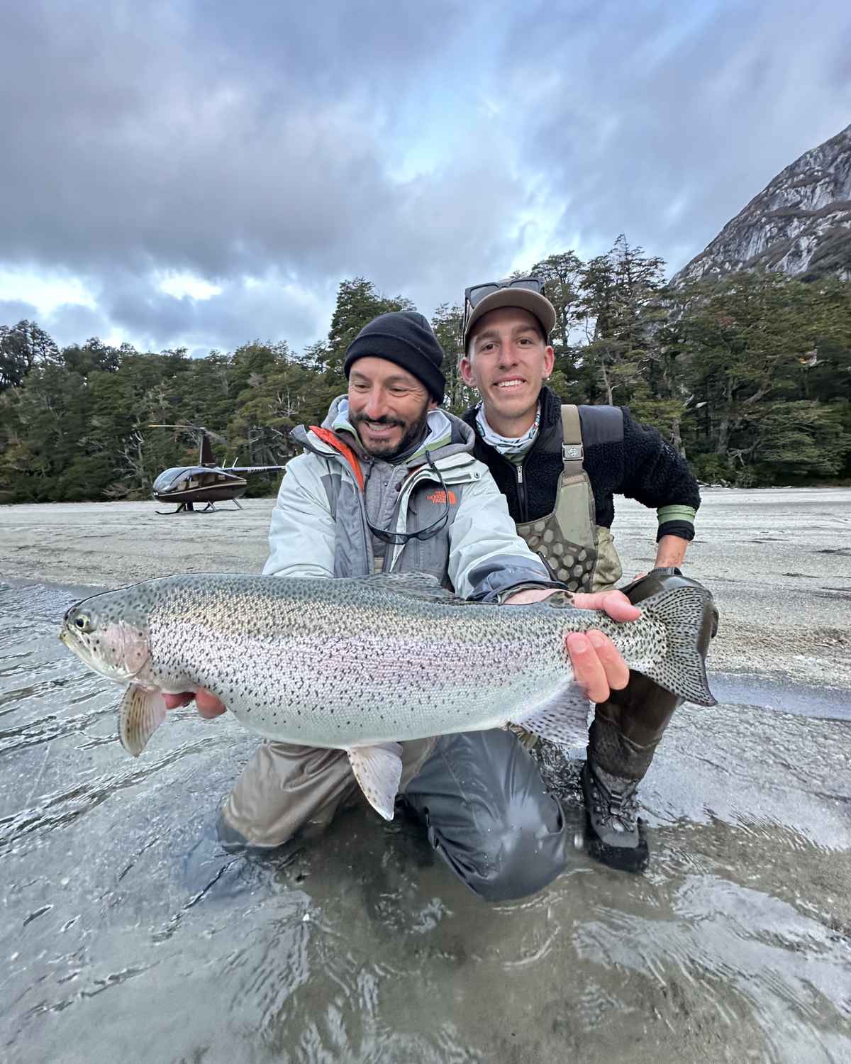 Pescadores con trucha arcoíris y helicóptero al fondo