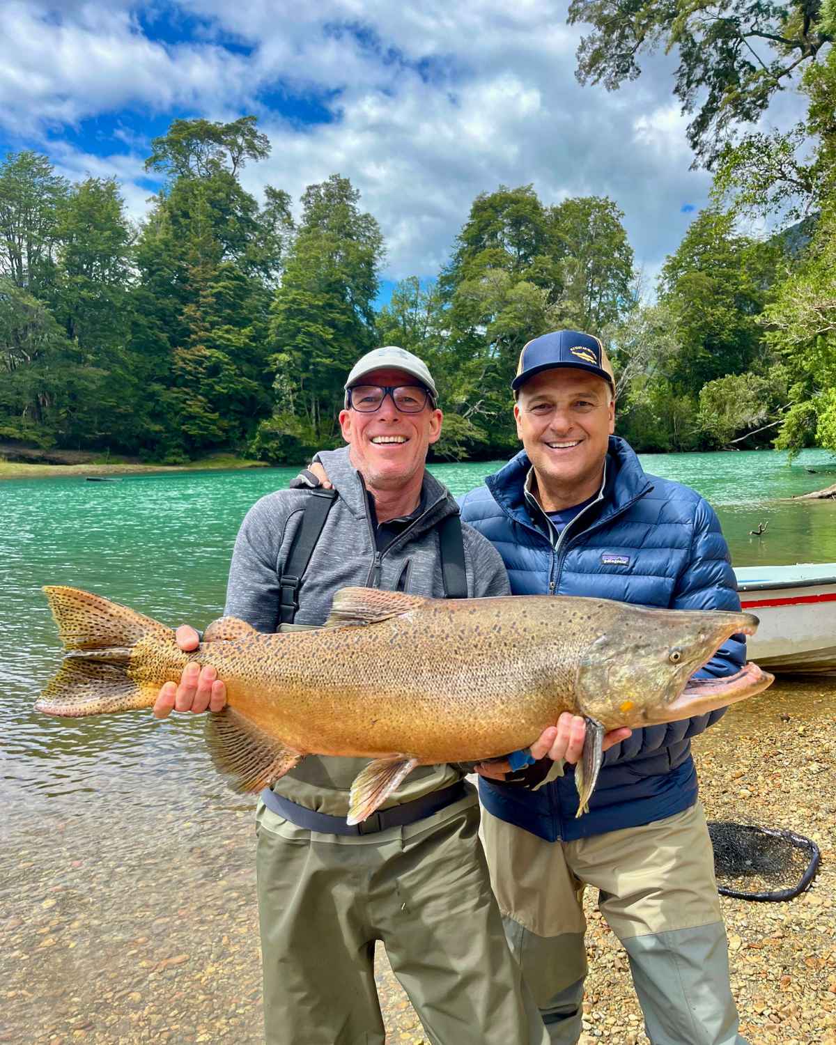Dos pescadores sonrientes sosteniendo un enorme salmón Chinook a orillas del río